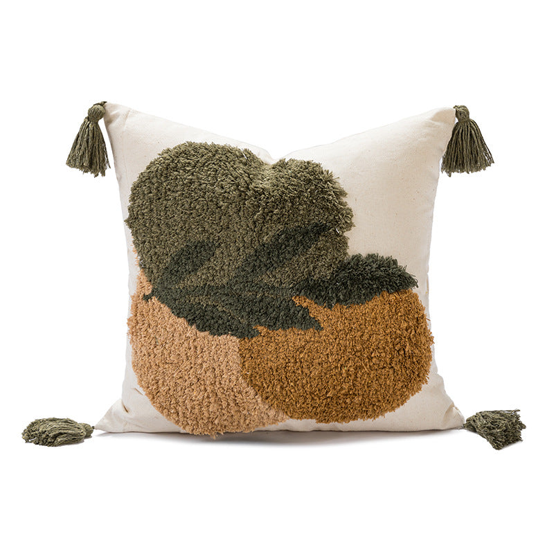 A square throw pillow with a textured, shaggy abstract design featuring a dark olive green leaf motif over a warm tan and light beige background, finished with matching tassels on the corners.